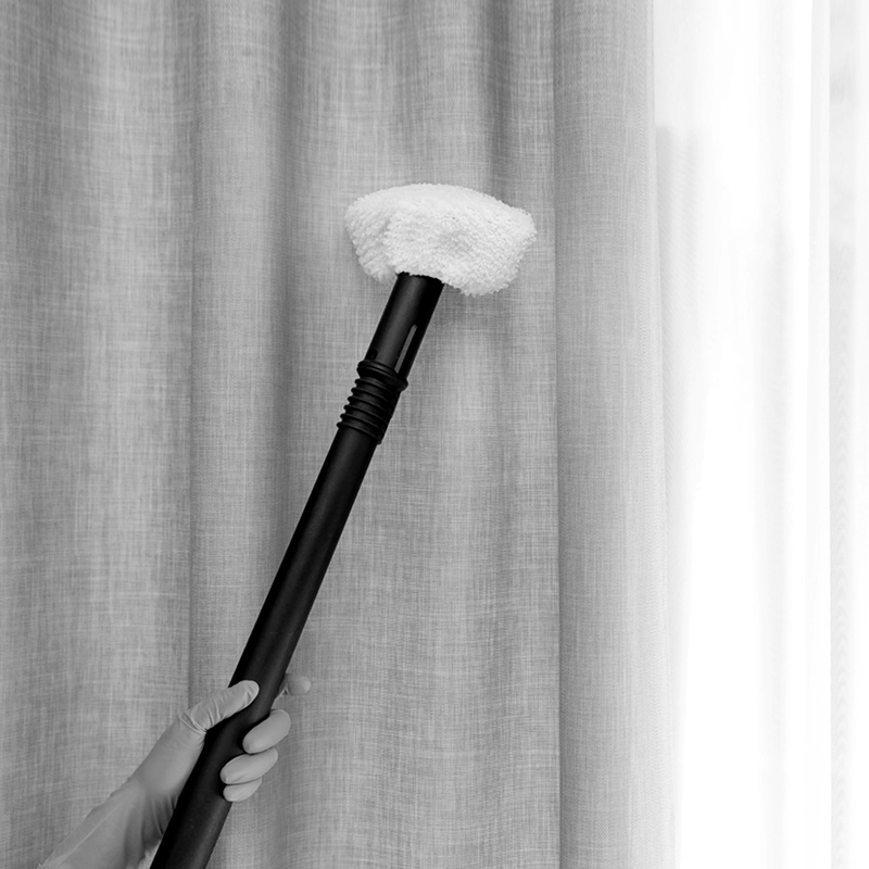 Hand removing dust from curtain with steam cleaner indoors